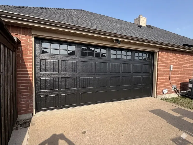 Black raised panel steel garage door on a red brick home