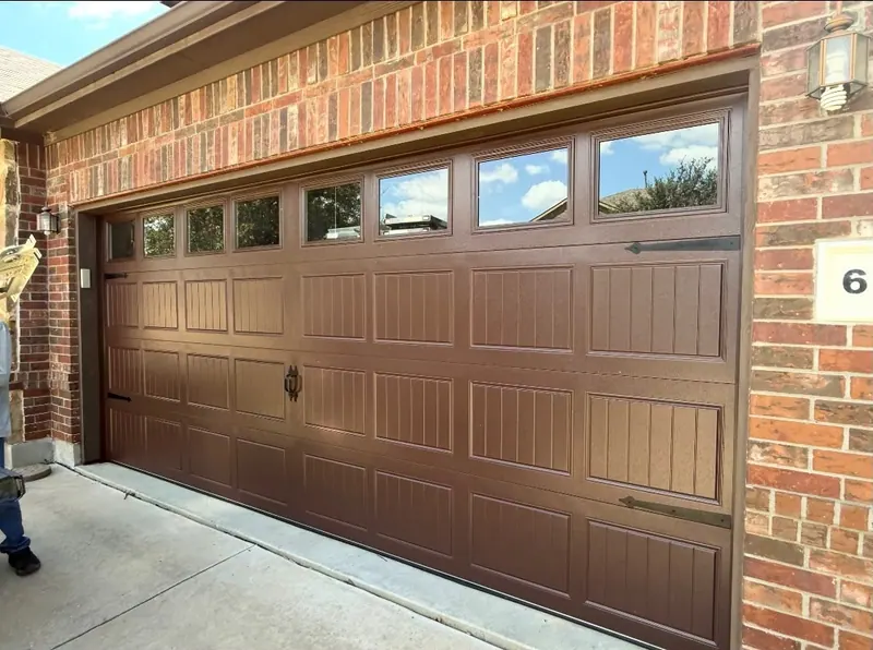 Brown carriage house garage door with decorative windows on a brick home