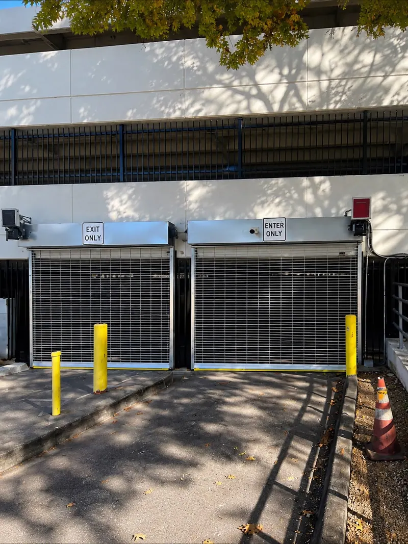 Two commercial rolling steel grille doors at a parking garage entry with enter and exit lanes