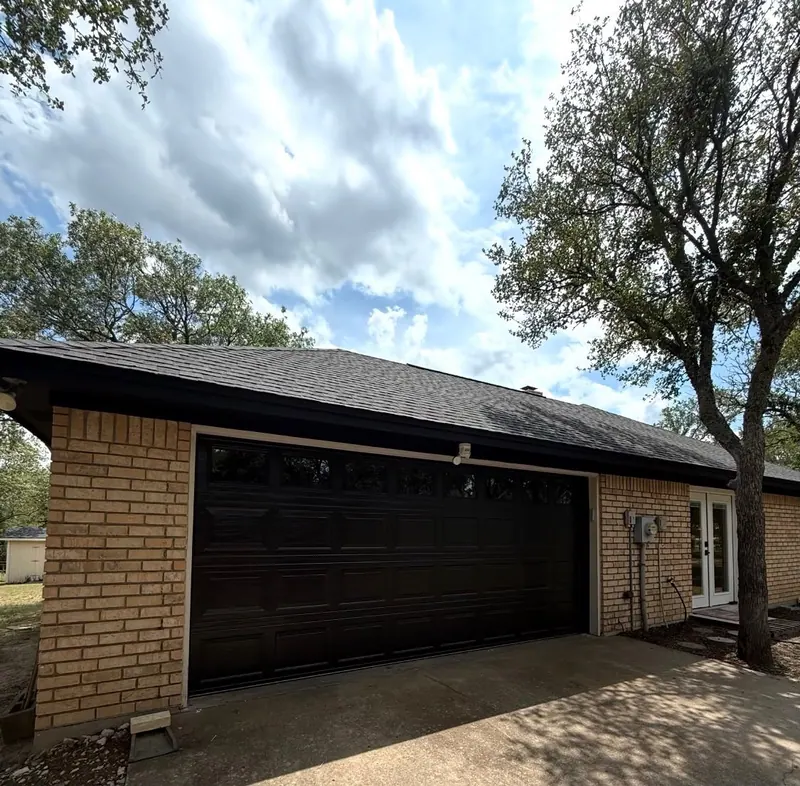 Dark stained wood garage door on a single story ranch home with mature trees