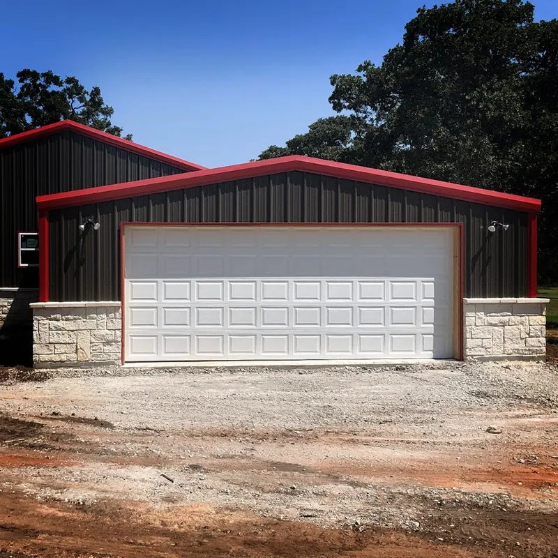 White garage door on a metal building with red trim and stone base