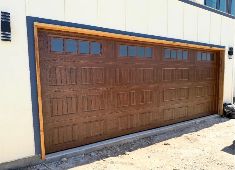 Stained wood look carriage garage door with windows on a white home