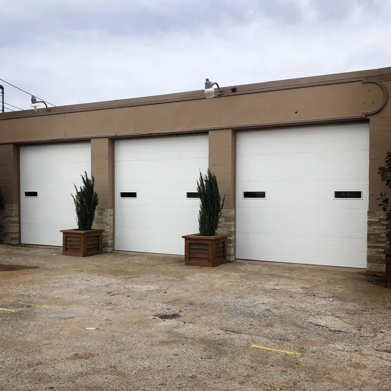 Three white commercial garage doors with planters between them